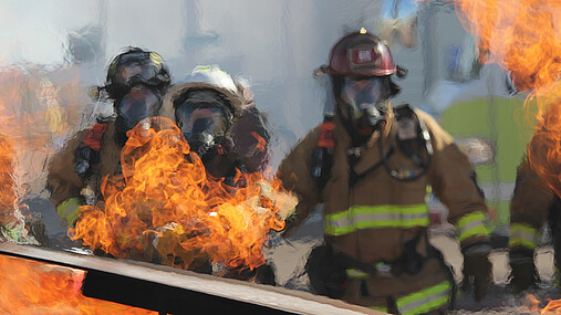 Foto zum Thema Bundesamt für Bevölkerungsschutz und Katastrophenhilfe (BBK): Im Vordergrund sind Flammen zu sehen, im Hintergrund Feuerwehrleute mit Atemschutz.