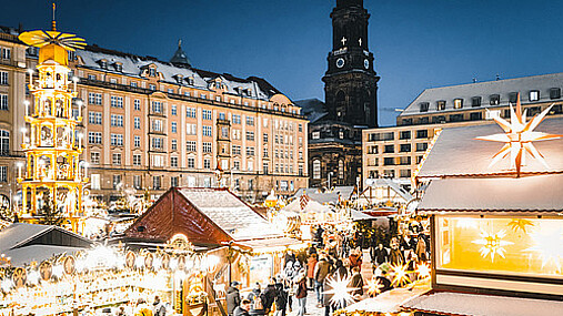 Foto zum Thema "Dresdner Striezelmarkt": Zu sehen ist der Markt, die Lichter leuchten in der Dunkelheit. Links im Bild ist die Weihnachtspyramide.