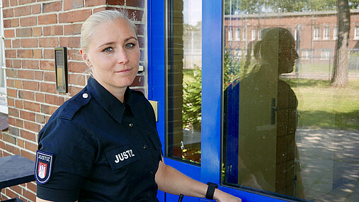 Foto zum Thema "JVA Hahnöfersand": Zu sehen ist Justizvollzugsbeamtin Dammann. Sie steht vor einer Tür und schaut in die Kamera.